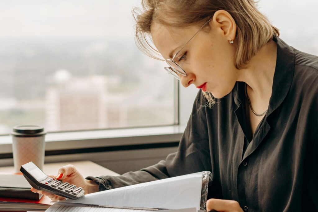 pexels photo 8297035 8297035 Businesswoman working with calculator and financial documents by window, focused and analytical.